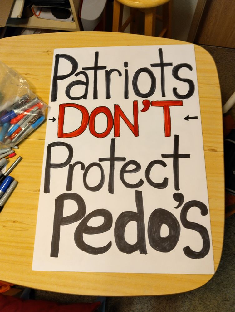 A large poster board is on a table strewn with markers. The poster board reads: Patriots don't protect pedo's