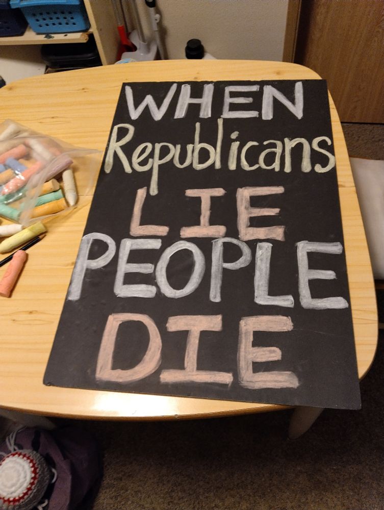 Chalk is spread on the left side of a small table. A large poster fills the table. On the poster these words are written: When Republicans Lie People Die