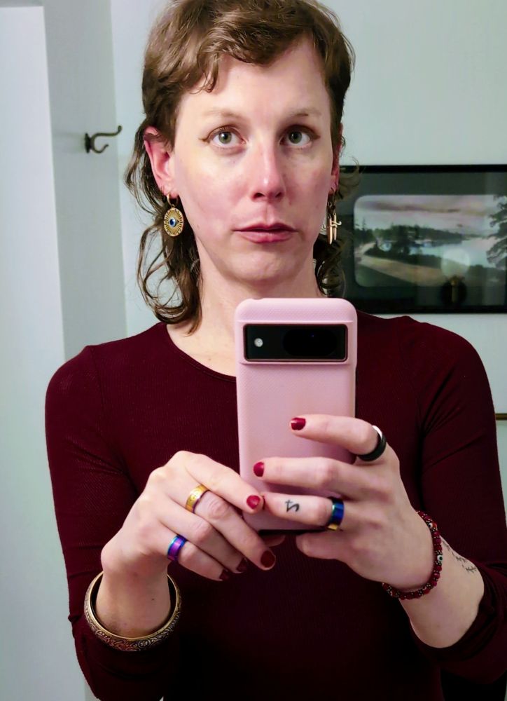 Mirror torso selfie; a grown woman in a maroon dress. Chromatic rings. Red fingernail polish. Faux gold earrings.