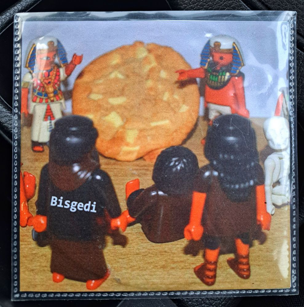 A CD of the album Bisgedi by the band Bisgedi. On the cover half a dozen PlayPeople dressed as Egyptians worship a white chocolate chip cookie.