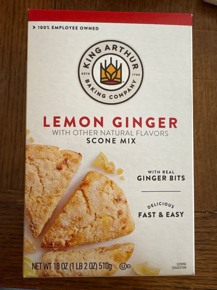 A box of King Arthur Lemon Ginger Scone Mix. The box is white with the ted& gold King Arthur crown logo, red pattering and several golden brown triangle scones.