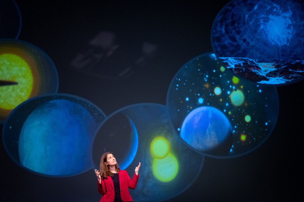 Natalie Batalha on stage speaking with a creative graphic being projected behind her 