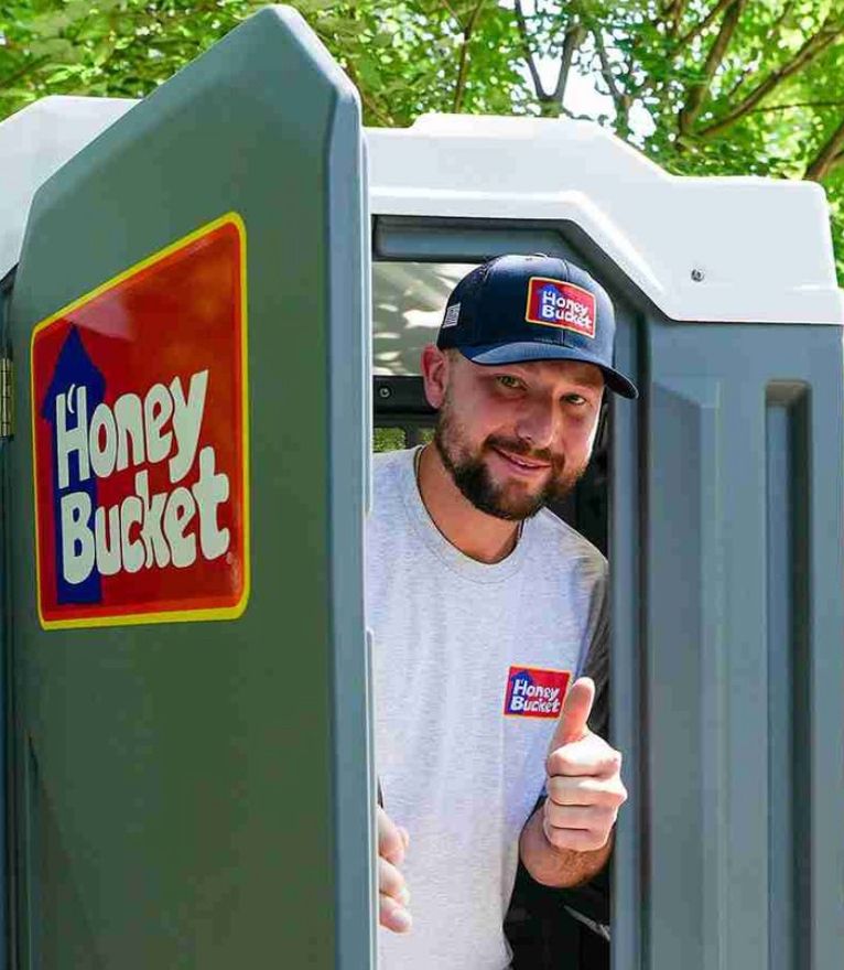 Honey Bucket portapotty promotional image showing a man smiling and giving a thumbs up from a portapotty