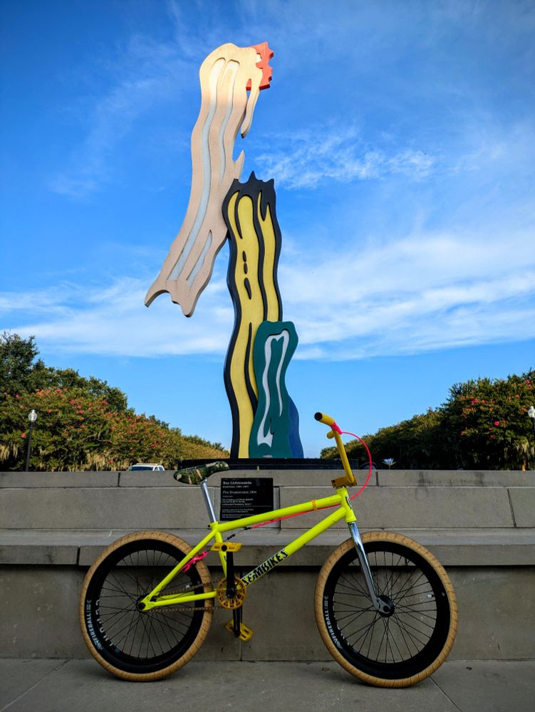 yellow bike parked in front of a Roy Lichtenstein sculpture 