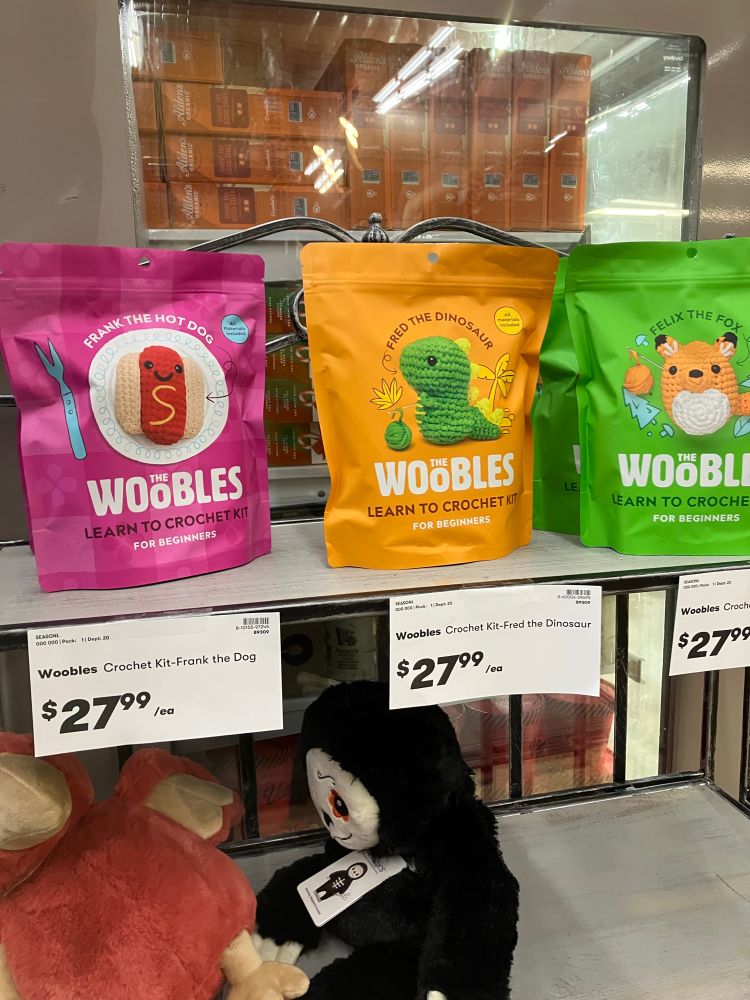 A store shelf with beginner crochet kits to make a stuffed animal hot dog, dinosaur or fox