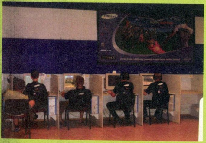 another phoito of teenagers, wearing head sets and what looks like black samsung branded t-shirts, are sitting in internet cafe cubicles, competing in the world cyber games (line of cubicles against a wall).