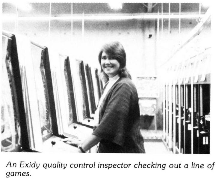 black and white photo of a woman (head turned to the side, smiling at the camera) testing the quality of a line of exidy's upright machines. she is standing inbetween two long lines of uprights.
caption: an exidy quality control inspector checking out a line of games.

