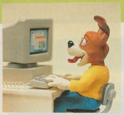 clay(?): a cute dog with its tongue out, wearing a yellow top and blue pants, is sitting at a computer, hands on the keyboard.