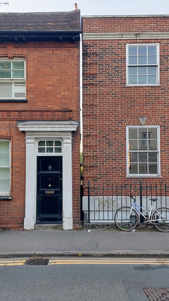 A photo of two brick-built 2-storey buildings taken from the road. They are separated by a very narrow gap of about 4 inches through which you can see daylight.