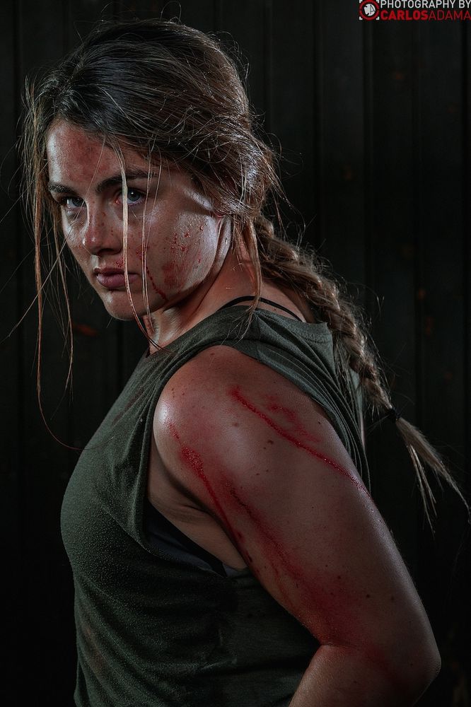 Nieke cosplaying Abby Anderson. She is looking over her shoulder back at the camera. Her biceps are fire.