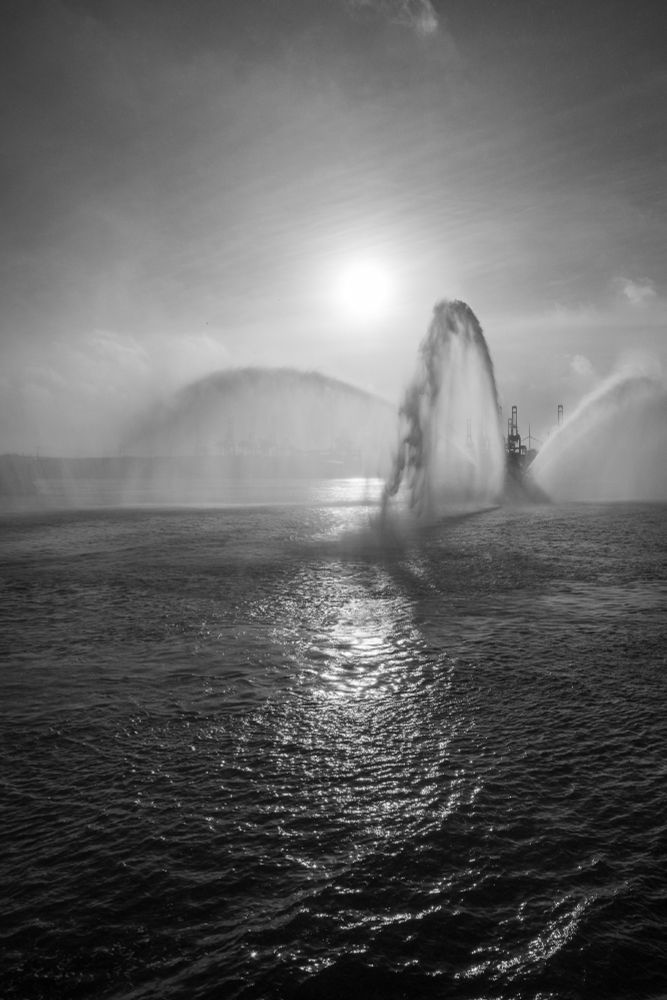 Schwarzweißfoto eines Feuerwehrschiffes mit Fontäne im Hamburger Hafen