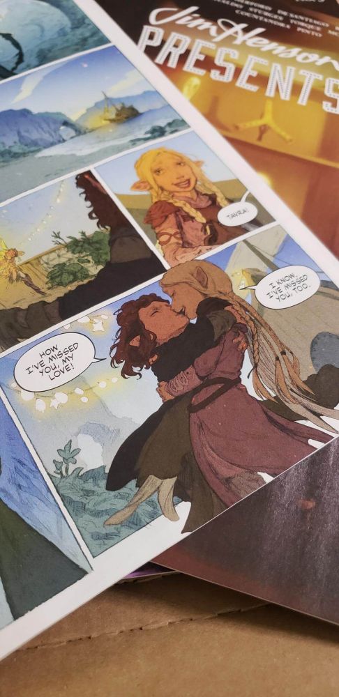 photograph of a comic page showing onica and tavra from the dark crystal: age of resistance, embracing and kissing, saying "How I've missed you, my love!" and "I know. I've missed you, too."