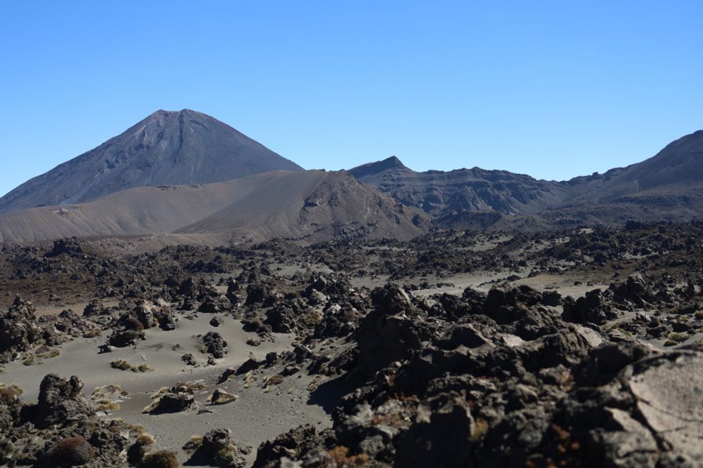 a sandy desert with volcanic rocks in the foreground and mount ngauruhoe in the background