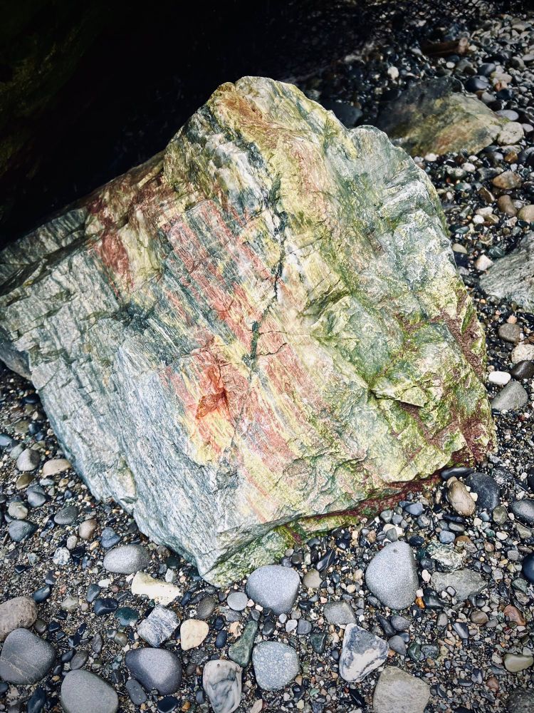 Striated rock on a pebbly beach with grey, red, yellow, and green stripes