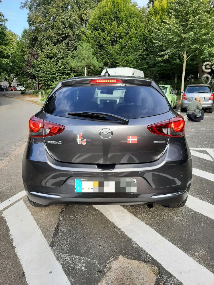Mazda 2 Homura in matrixgrau ; Heckansicht mit Dänemark-Aufklebern. Rechts: Flagge, links Silhouette vom Land in Flaggenfarbe