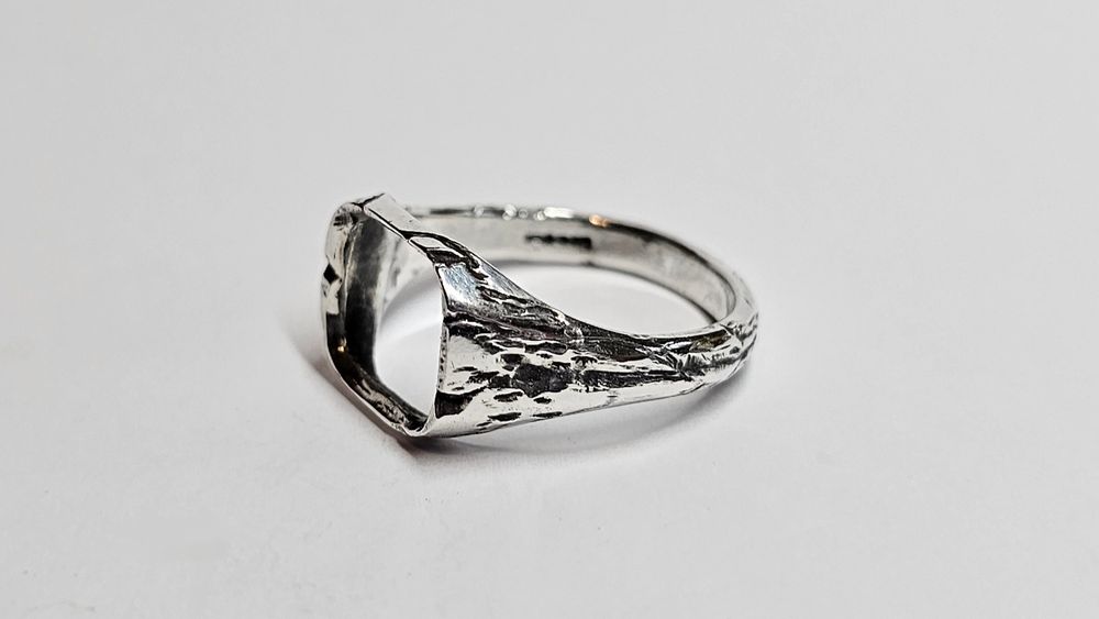 A silver ring with deep, ragged carved lines that look a bit like lightning. The ring has a large square opening for a face thus it is called a 'window' ring. 