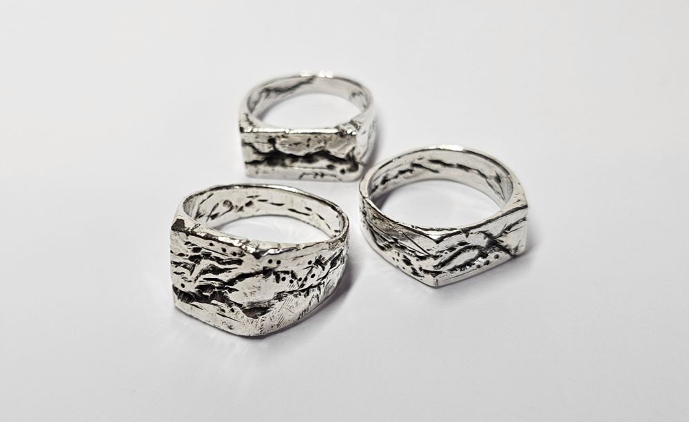 The Quake Ring is a chunky silver ring with a large flat face with deep rugged lines carved on every surface including the inside of the rings.