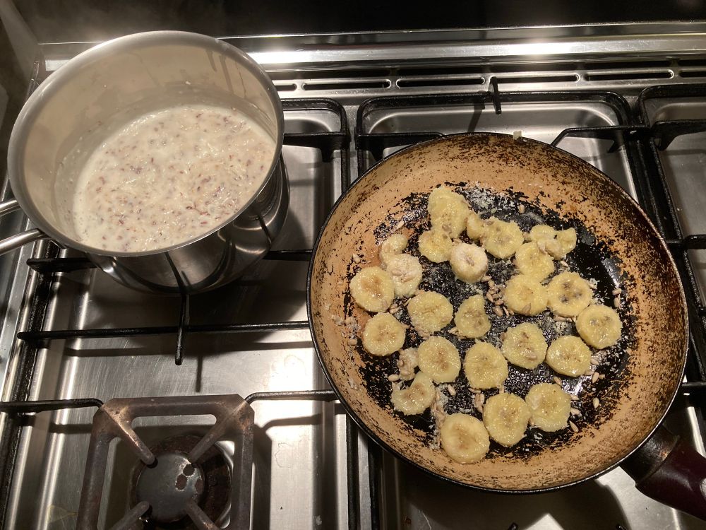 Foto van de pan met pap en de koekenpan met de banaan en kokos op ons rvs fornuis