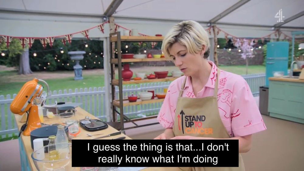 A screengrab of Jodie Whittaker in the Great British Bake Off tent. She is a white woman with short dyed blonde hair wearing a pink jumpsuit and a Stand Up to Cancer apron. The caption reads "I guess the thing is that... I don't really know what I'm doing."