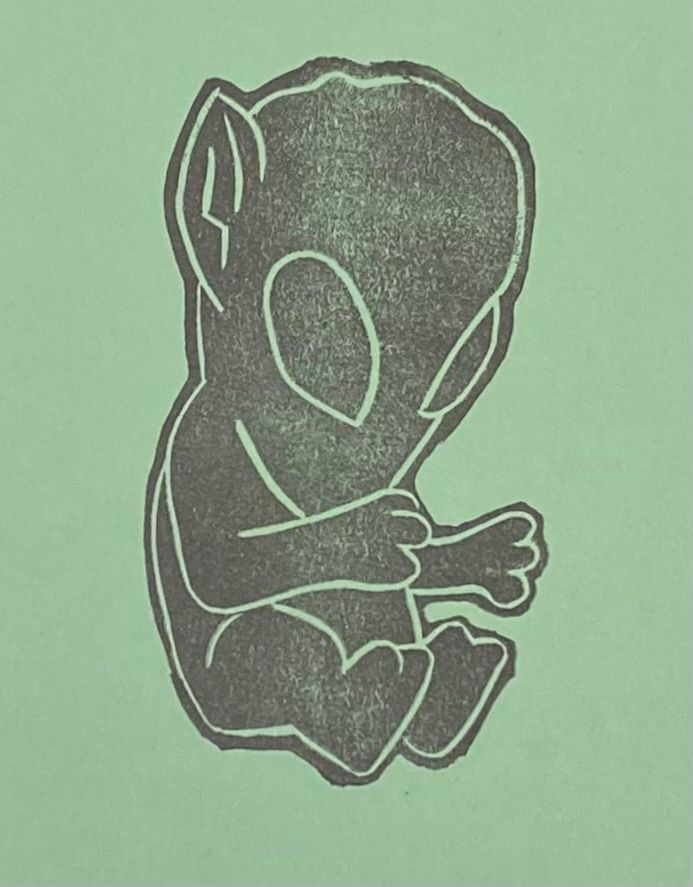 A linocut print of an alien egg toy on light green paper. 