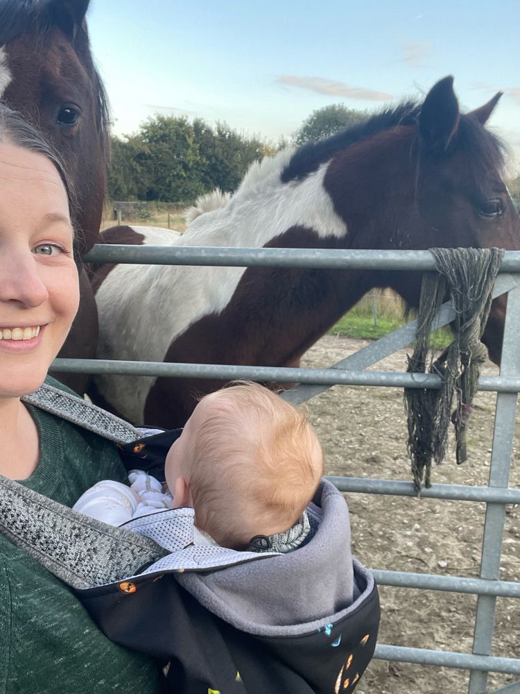 Me with my baby standing in front of some horses and smiling