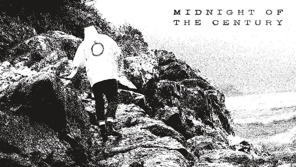 Midnight of the Century. Evocative black and white. A lone figure scrambles over a rocky shoreline, wearing a light-coloured coat with the Oroboro logo on it, a circle with a tick at the midnight position.