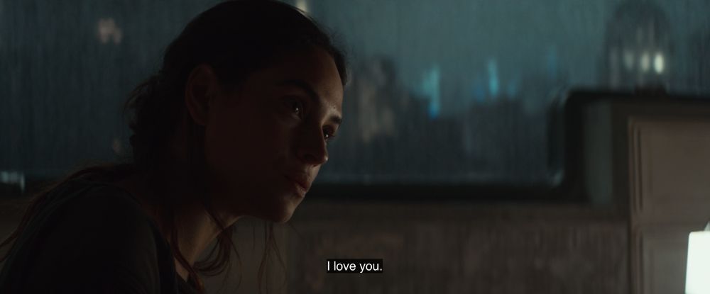 A still from Andor season 2 episode 4. It's nighttime, and Bix is sitting at the table in her and Cassian's apartment. She's looking at Cassian (off-screen) and saying, "I love you."