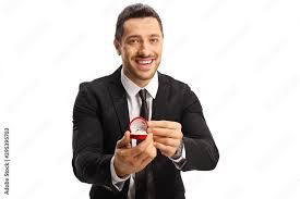 stock image of caucasian man in formal attire with a red box-encased ring proposing to camera
