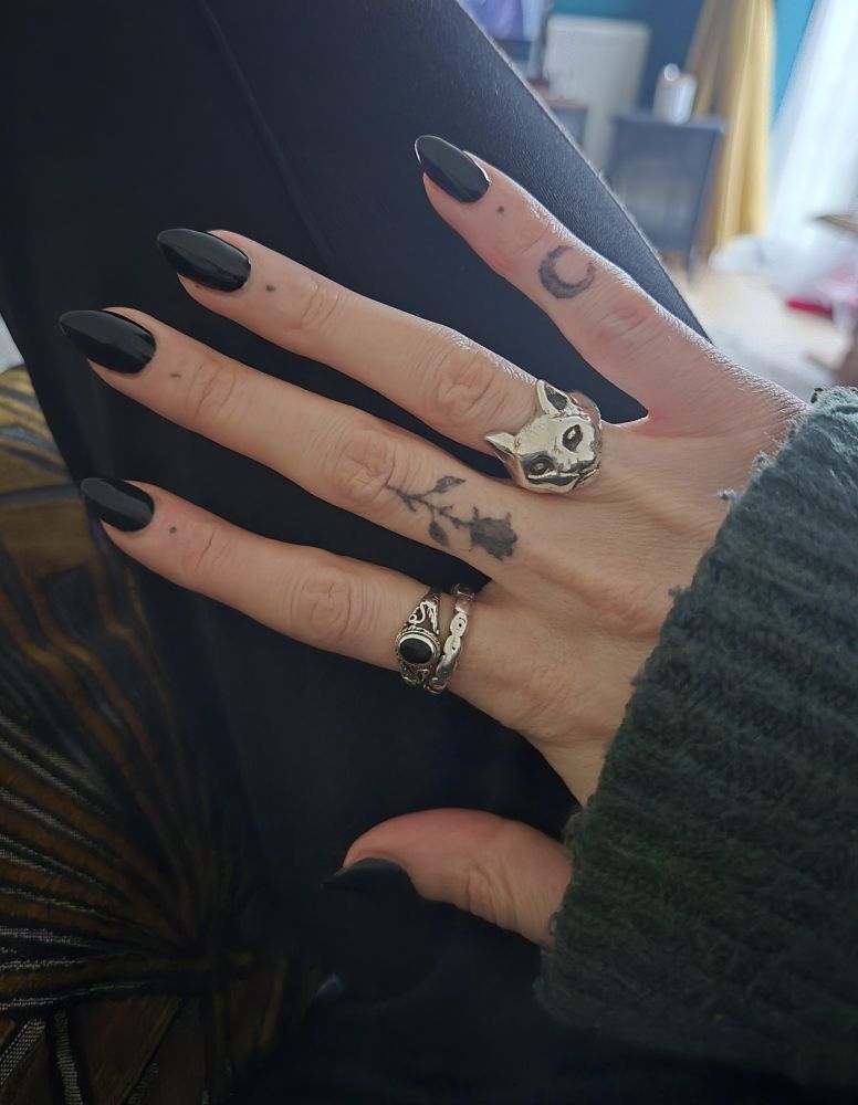 A hand with long black nails, silver rings and tattoos. 