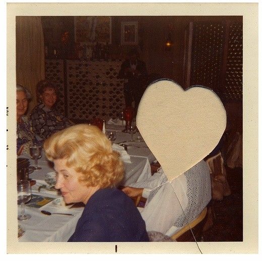 A picture that has been cut, a heart-shaped hole. A woman with a lovely blonde do, sits beside it. 
