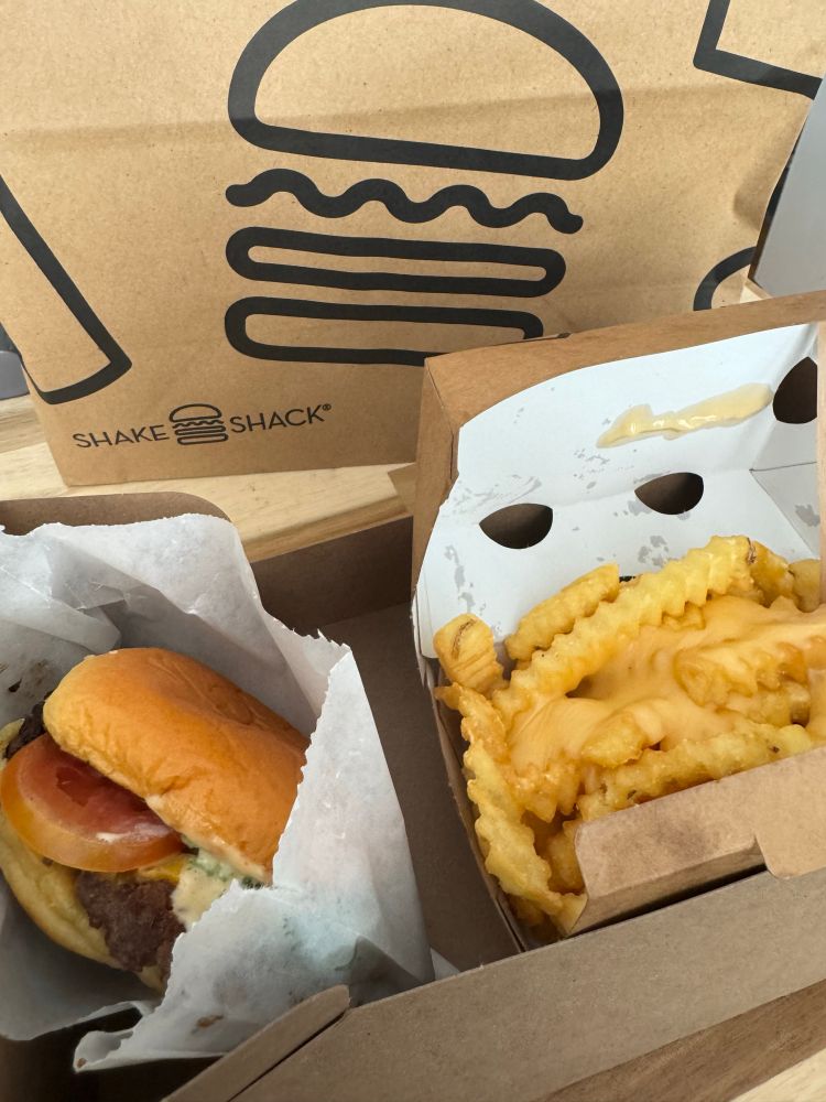 Shake Burger and crinkle-cut cheese fries in cardboard to-go packaging. 