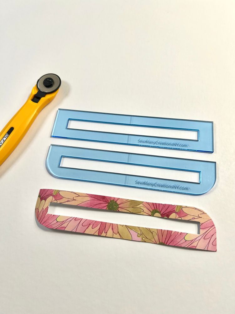 A yellow rotary cutter, two clear blue plastic zipper overlay templates that say SewManyCreations.com, and one pink floral vinyl zipper overlay. 