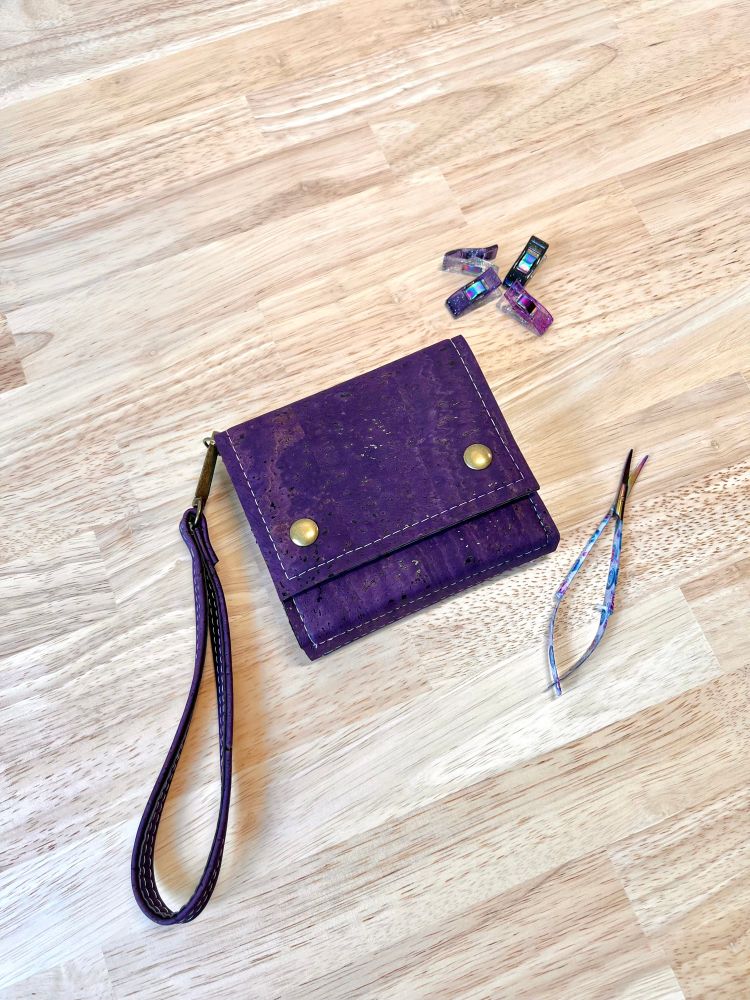A purple cork wallet with a wristlet strap on a butcher block counter