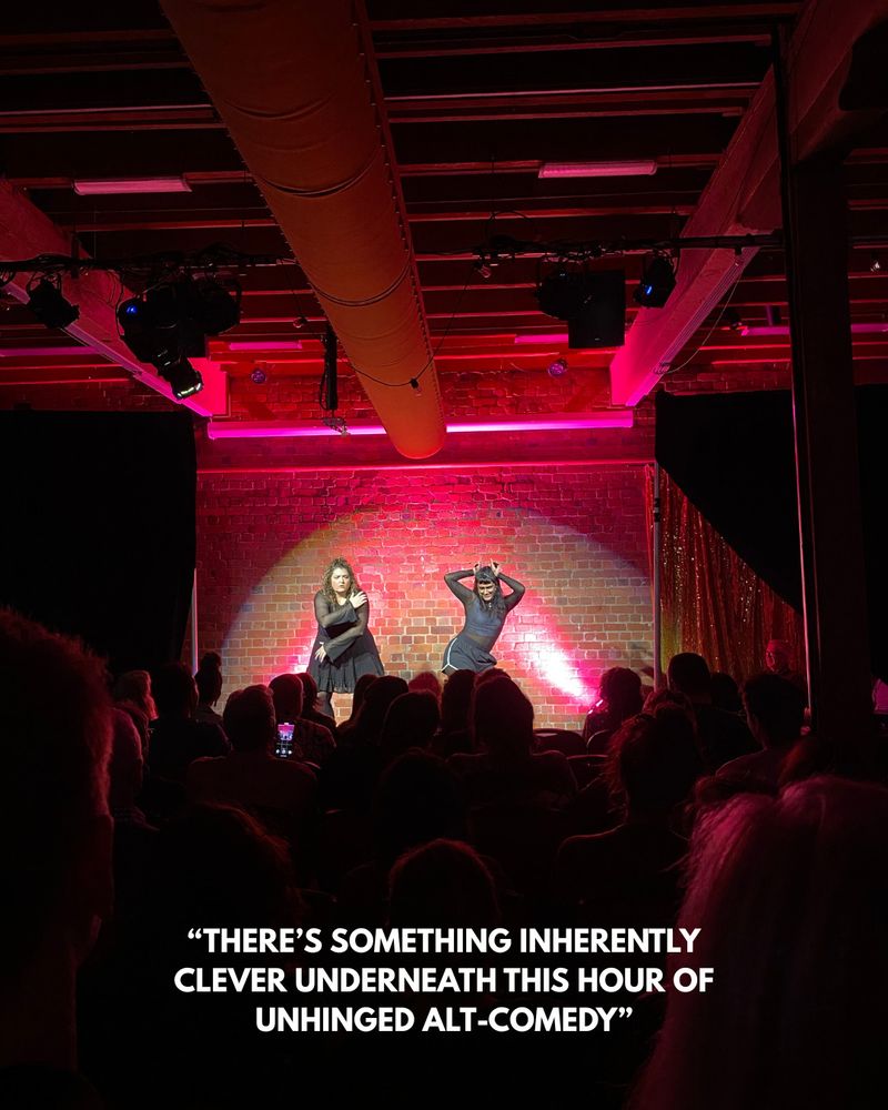 two women in front of the audience hold hands and strike a dramatic pose as if mid-dance