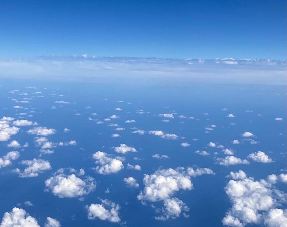 飛行機から見た海と空の写真。もこもこと小さな雲が広がっている。飛行機の高度が高く雲が下に見えるので空と海の境界がわからないような青い色。