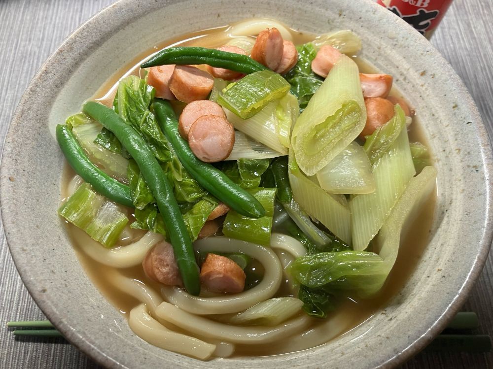 器に盛られたうどん。具はインゲンと長ネギと白菜と細かく切ったソーセージ。七味も用意した。お汁は味噌味で煮込んである。