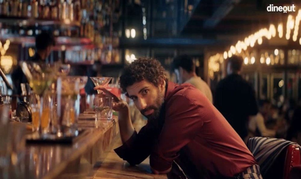 a man sitting at a bar with a martini in his hand and the word dineout on the bottom