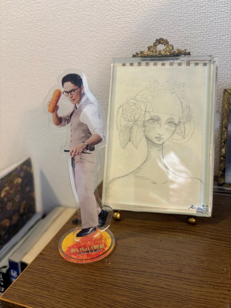 映画「おいしい給食 炎の修学旅行」公式グッズの甘利田先生アクリルスタンドと、ルアンちゃんが描いたクロッキー・アンリエットさんの写真です。