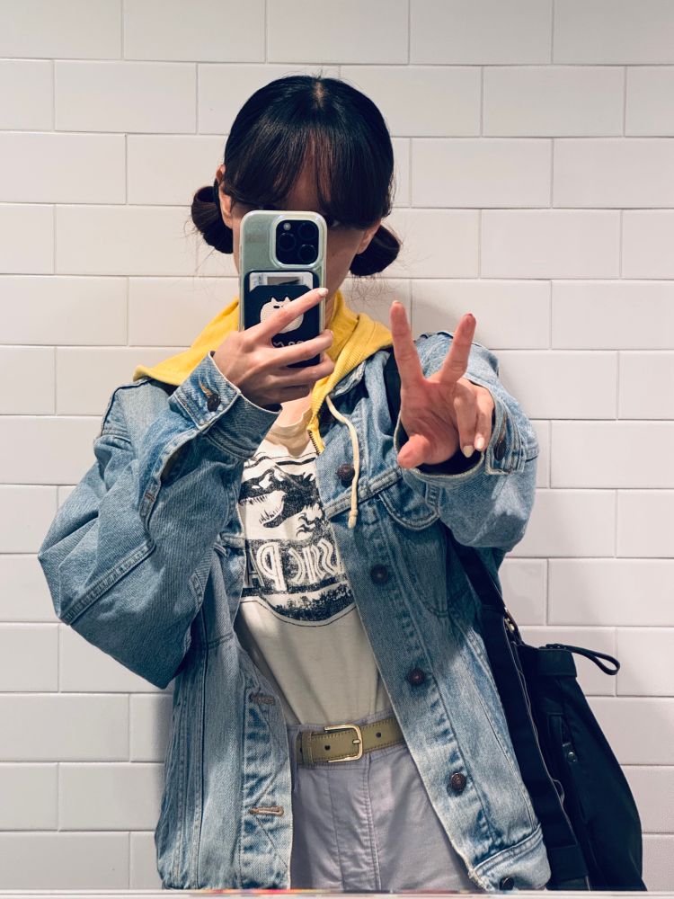 Photo of a person with buns wearing a denim jacket and doing peace sign into a mirror