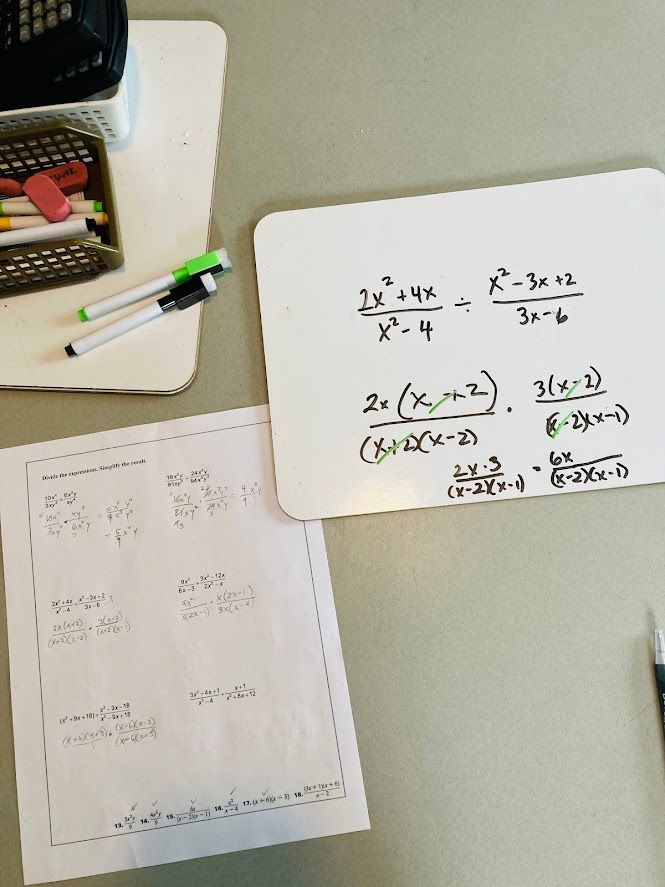 view of classroom table with white boards, markers, and a rational functions simplification problem written on a white board.