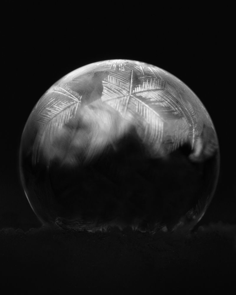 Black and white photography of a freezing soap bubble. Ice crystals have formed on the top half.