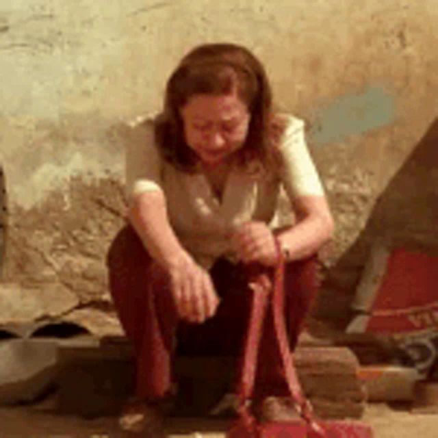 a woman is squatting down on the ground holding a red purse .