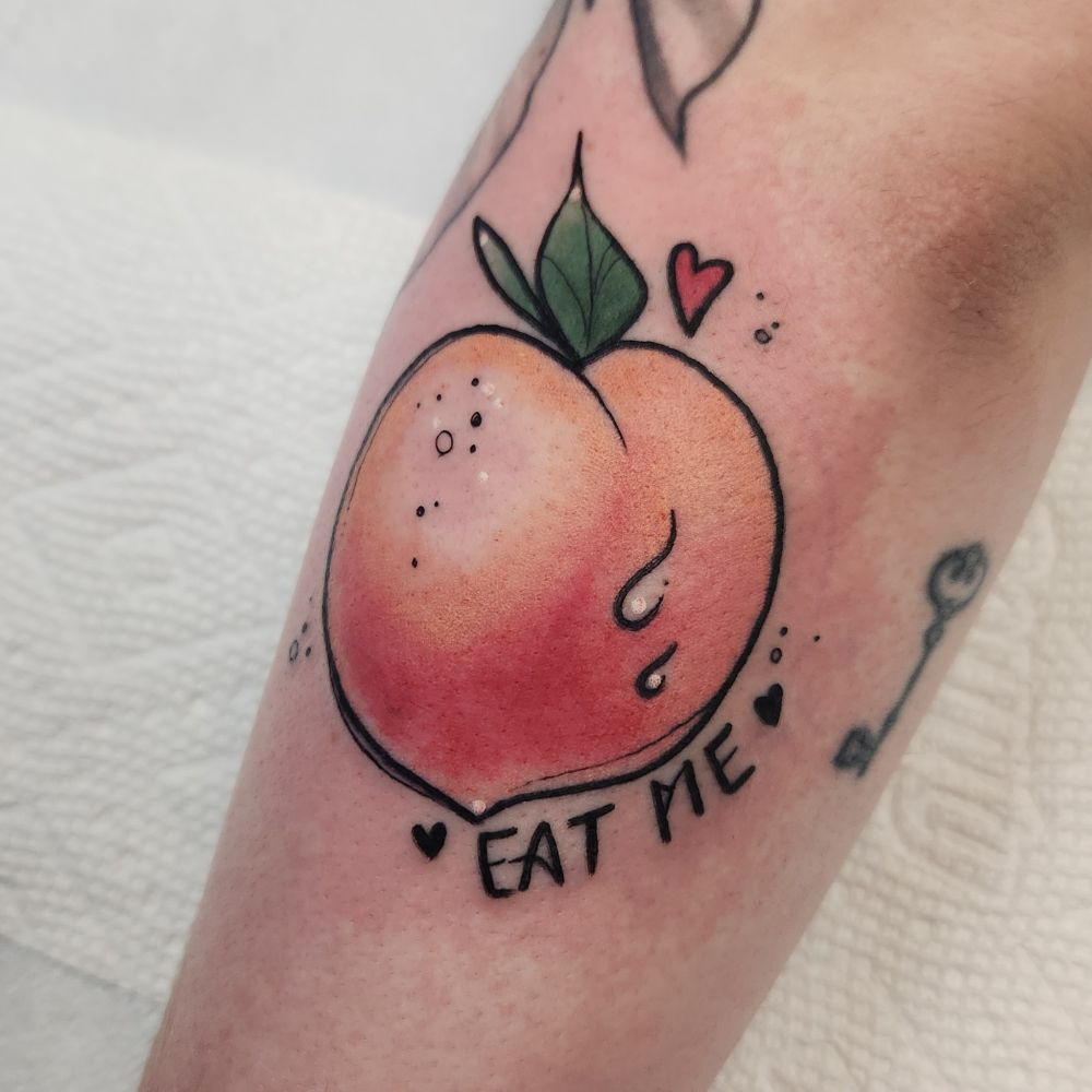Tattoo of a peach that says "eat me" with hearts