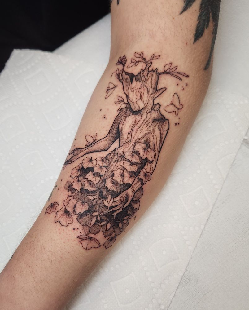 Blackwork tattoo of a wood tree spirit from dragon age Veilguard, leaves growing from it with ivy crawling up. 