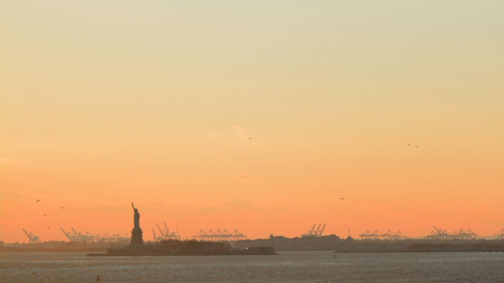 photo from 11/2022 of the statue of liberty silhouetted on an orange gradient horizon at dusk