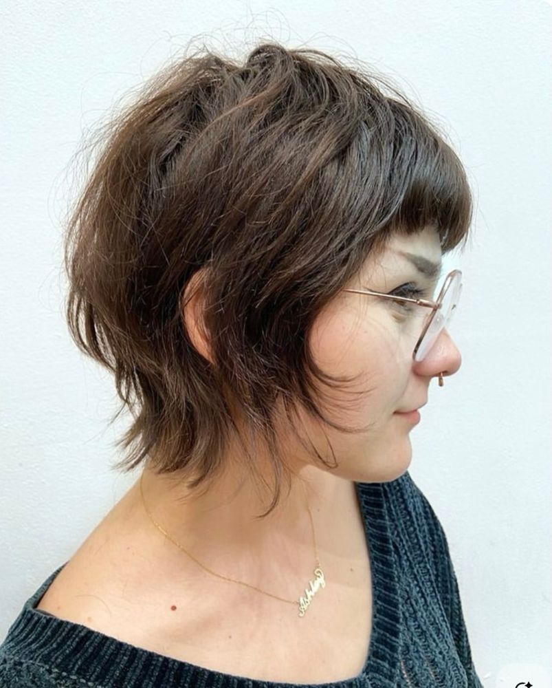 A woman facing to the side with brown hair that's a little bit wavy and comes down just to the nape of the neck. It's kind of a take on a bob hairstyle with thin, wispy ends.