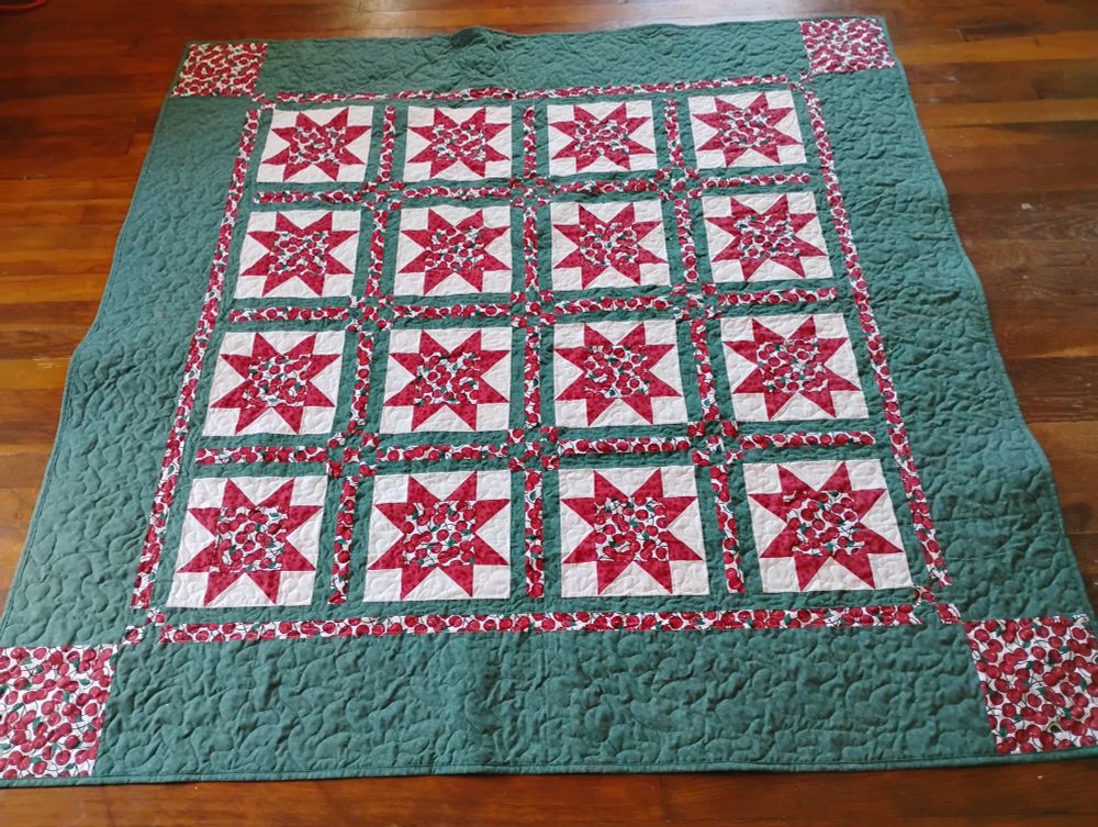 Variable star blocks (4 blocks x 4 rows) with a red/white cherry print center and red points, green sashing and border, with cherry print squares in the four corners. It's about 60" square.