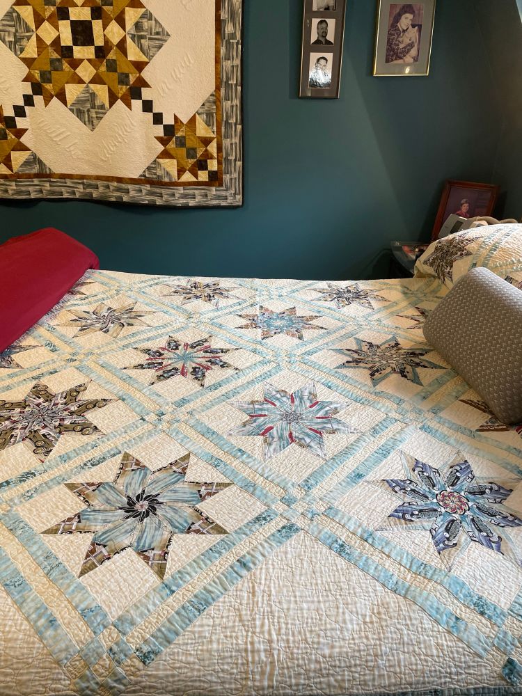 Kaleidoscope style quilt in turquoise on cream background shown against teal wall.