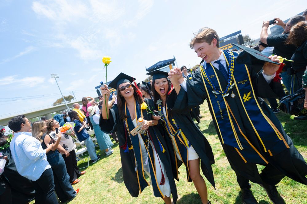 Graduates from UC San Diego celebrating outdoors with diplomas in hand, smiling and tossing graduation caps.