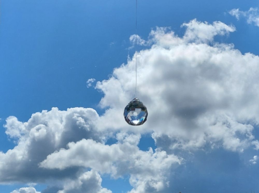 Blauer Himmel mit weißen Wolken, davor eine kleine geschliffene Glaskugel in der sich Himmel und Wolken spiegeln